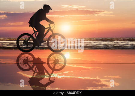 Silhouette di un ciclista in spiaggia con cielo drammatico durante il tramonto Foto Stock