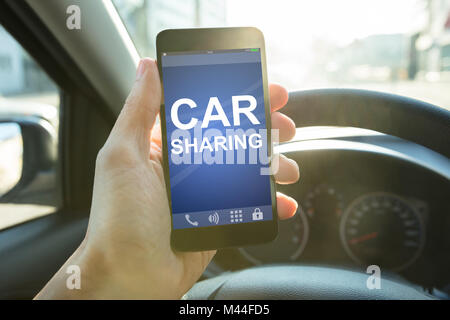 Primo piano della mano d'uomo azienda smart phone con car sharing app sullo schermo in auto Foto Stock