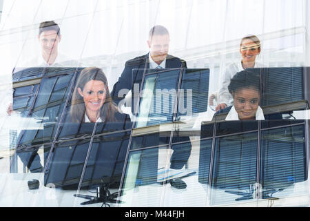 Multietnica gente di business utilizzando i computer desktop in ufficio visto attraverso il vetro Foto Stock