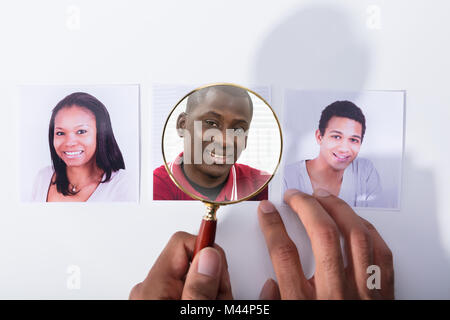 Close-up di un imprenditore la mano che tiene la lente di ingrandimento su maschio africana del richiedente Fotografia Foto Stock