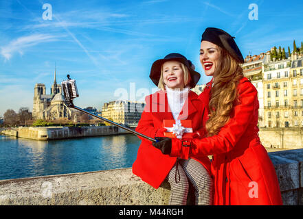 Luminose a Parigi. alla moda di madre e bambino i viaggiatori in rosso strati sul terrapieno a Parigi, in Francia con il regalo di Natale box prendendo selfie utilizzando selfie Foto Stock