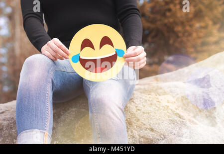 Ridendo emoticon con lacrime di gioia. Donna con divertimento fuori e tenendo un allegro carta stampata Smiley face. Comunicazione felice e sorridente icona. Foto Stock