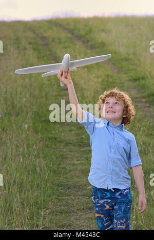 Little Boy tenendo un aeroplano in legno modello sul campo Foto Stock