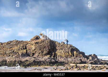 Un uomo di arrampicata su roccia della cappella sulla spiaggia a Perranporth in Cornwall Regno Unito. Foto Stock