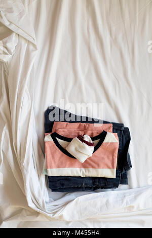 Angolo di alta vista di ripiegata di T-shirt, un paio di calze e un paio di pantaloni sulle bianche lenzuola di un letto disfatto, con qualche spazio vuoto sulla parte superiore Foto Stock