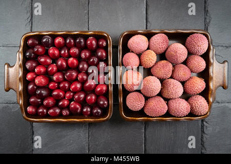 Cranberries accanto al litchi frutta - due quadrati, disposti simmetricamente ciotole di frutta Foto Stock