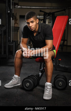 Giovane uomo seduto su un banco di lavoro in palestra Foto Stock
