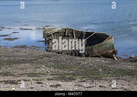Gravemente devastata in legno barca di pesca abbandonato ricoperto di alghe e di marciume lontano sulla spiaggia. Foto Stock