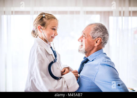 Senior medico e una piccola ragazza con uno stetoscopio nel suo ufficio. Foto Stock