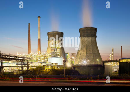 Una raffineria di petrolio con due torri di raffreddamento e il blu del cielo notturno. Foto Stock