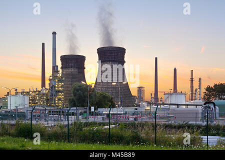 Una raffineria di petrolio con due torri di raffreddamento e colorata del cielo della sera. Foto Stock