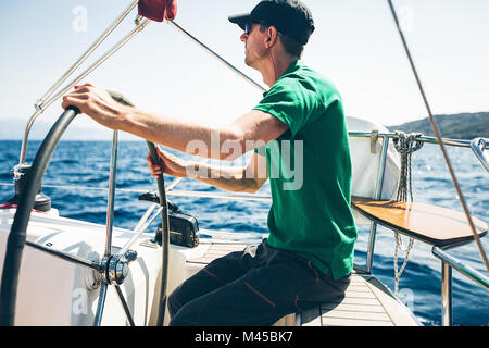 Metà uomo adulto yacht di sterzo in prossimità della costa, Croazia Foto Stock
