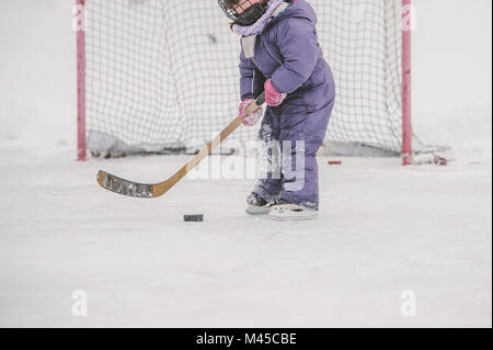 Ragazza giovane la riproduzione di hockey su ghiaccio, preparando a colpire il puck, metà sezione Foto Stock