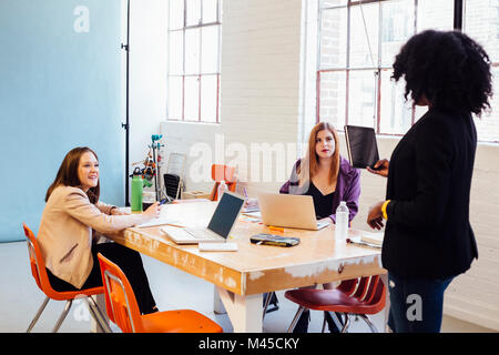 Donna con tavoletta digitale parlando ai colleghi di lavorare alla scrivania Foto Stock