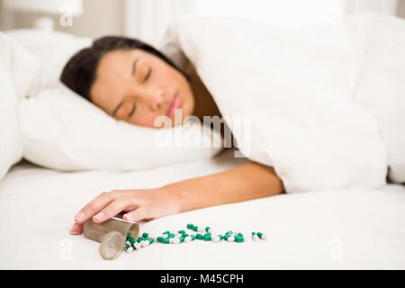 Brunette dormire nel letto dalla fuoriuscita di una bottiglia di pillole Foto Stock