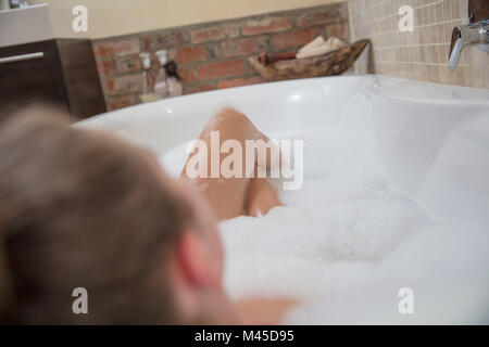 Sulla spalla vista della giovane donna reclinata in bagno di bolle Foto Stock