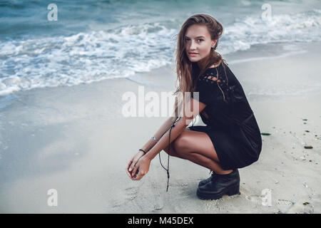 Ritratto di giovane donna accovacciata da bordo d'acqua sulla spiaggia, Odessa, Oblast di Odessa, Ucraina Foto Stock