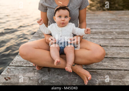 Madre seduta zampe trasversale sul lago di pier con la nostra bambina sul giro, ritagliato Foto Stock