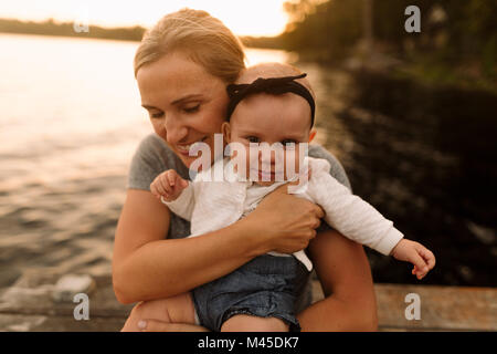 Madre seduta sul molo abbracciando la nostra bambina Foto Stock