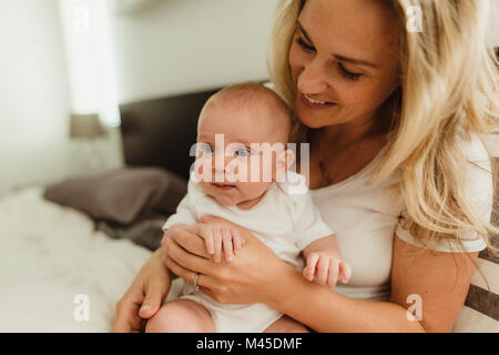 Baby ragazza seduta sulla madre di giro sul letto Foto Stock