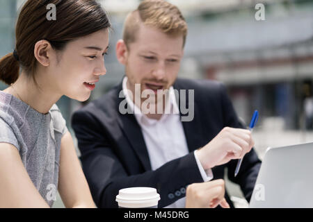 Giovane imprenditrice e un uomo guarda il computer portatile presso cafè sul marciapiede Foto Stock