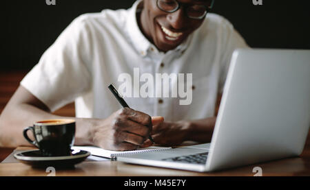 Il freelance scrivere note seduti ad un tavolo da caffè. Felice l'uomo al lavoro sul suo computer portatile presso una caffetteria. Foto Stock