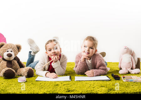 Adorabili Piccole sorelle di Disegno con matite di colore insieme sul pavimento isolato su bianco Foto Stock