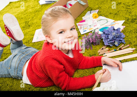 Sorridente bambina Disegno con matite di colore verde morbida moquette Foto Stock