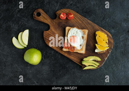 Vista superiore del toast con uova fritte e pomodori ciliegia per la prima colazione sul bordo di taglio Foto Stock