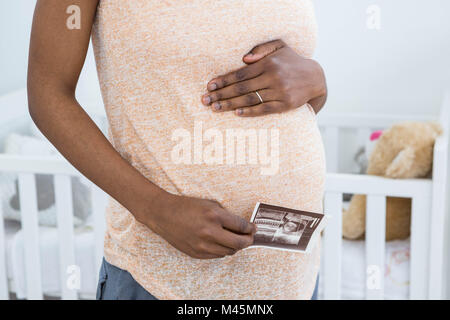 Donna incinta holding di scansione ad ultrasuoni vicino a culla baby Foto Stock