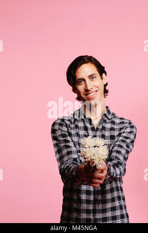 Sweet guy in camicia a scacchi holding e offrendo bouquet di fiori bianchi Foto Stock