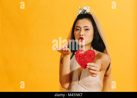 Sposa soffia un bacio e tenendo fuori un cuore rosso Foto Stock