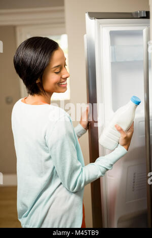 Sorridente brunette holding bottiglia di latte con frigorifero aperto Foto Stock