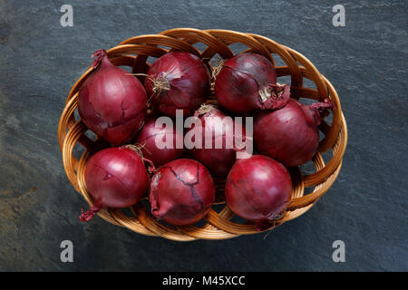 Le cipolle rosse nel cesto di vimini sulla tavola di ardesia top Foto Stock