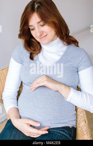 Attesa, bambino nascita, il concetto di famiglia. vi è una donna attraente con delicato sorriso e i capelli morbidi di tinta castagno, è incinta, e tenere premuto Foto Stock