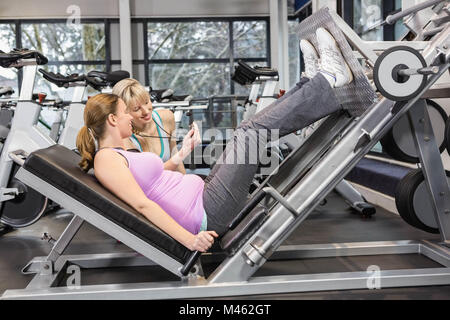 Trainer per motivare la donna incinta mentre utilizzando leg press Foto Stock