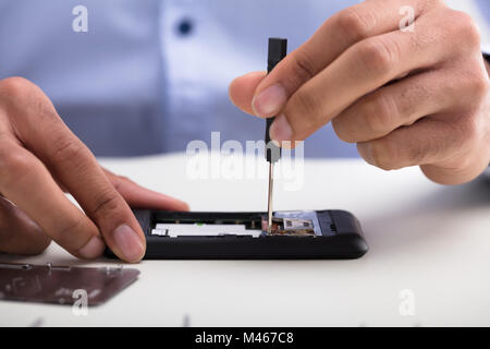 Close-up di un tecnico la mano la riparazione cellulare sulla scrivania Foto Stock