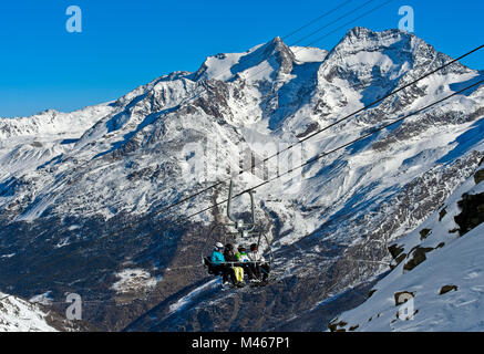Gli sciatori sulla seggiovia Längfluh, picchi e Fletschhorn Lagginhorn dietro, Saas fee, Vallese, Svizzera Foto Stock