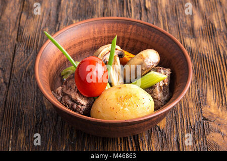 Stufato di carne con verdure in un tegame di coccio. funghi, carote, pomodori, sedano, cipolla. orizzontale Foto Stock