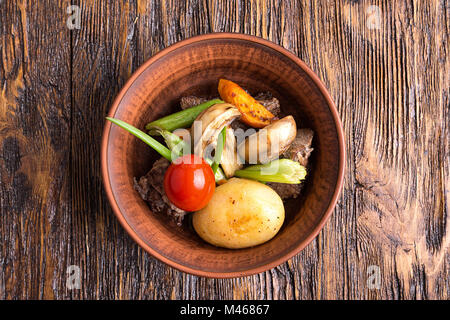 Stufato di carne con verdure in un tegame di coccio. funghi, carote, pomodori, sedano, cipolla. vista superiore Foto Stock
