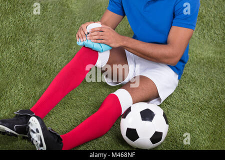 Close-up di un maschio ferito giocatore di calcio l'applicazione di ghiaccio sul ginocchio Foto Stock