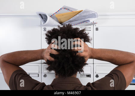 Vista posteriore di un giovane uomo che guarda la cassetta postale sovraccaricato con messaggi di posta indesiderata Foto Stock