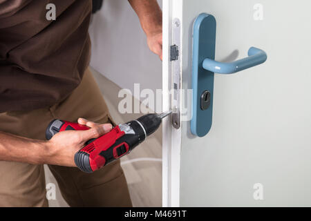 Carpenter Installazione serratura della porta con un cacciavite senza fili Foto Stock