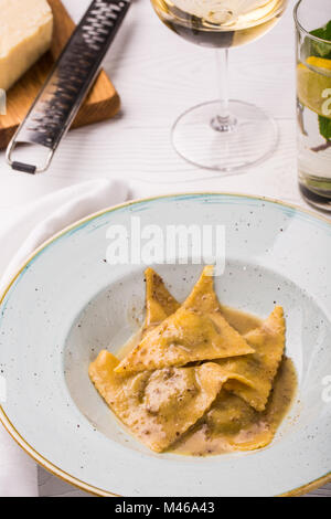 Ravioli di pasta con basilico e parmigiano sulla piastra. Parmigiano con una grattugia su un tagliere. Vino bianco e limonata. foto verticale Foto Stock