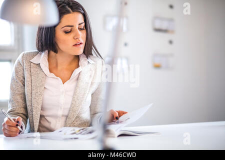 Imprenditrice leggendo la brochure tenendo note in Office Foto Stock