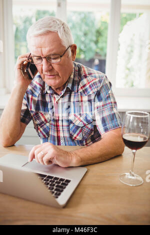 Preoccupato senior uomo prendendo sul telefono durante l'utilizzo di laptop Foto Stock