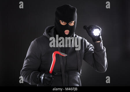 Ritratto di un ladro con torcia e palanchino su sfondo nero Foto Stock