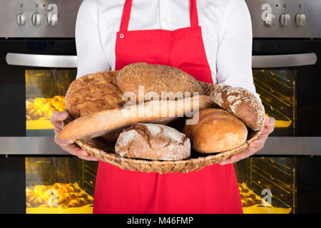 Persona mano che trattiene la piastra di vimini pieno di vari tipi di pane e panini di fronte al forno Foto Stock
