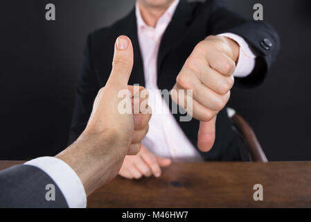 Due imprenditori che mostra le mani pollice in alto e il pollice verso il basso sulla Scrivania in legno Foto Stock