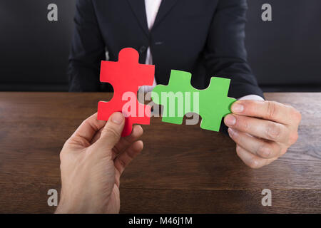 Close-up di due imprenditori unire pezzi di puzzle sulla scrivania in legno Foto Stock